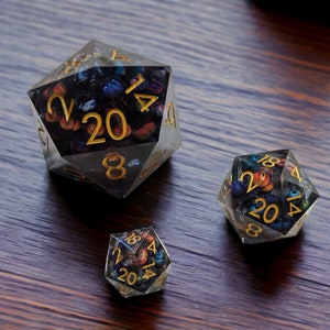 May include: Three clear, multi-sided dice with gold numbers and a colorful, abstract design. The dice are on a dark wood surface.
