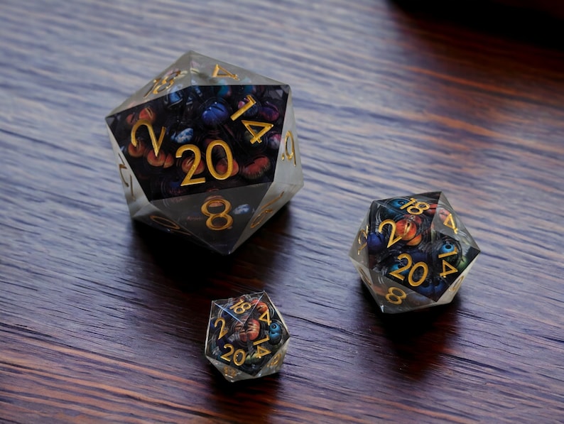 May include: Three clear, multi-sided dice with gold numbers and a colorful, abstract design. The dice are on a dark wood surface.