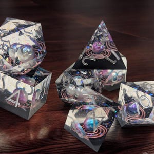 May include: Set of six iridescent dice with a galaxy theme. The dice are clear with embedded glitter and copper wire. Each die has a different number of sides, ranging from four to twenty.