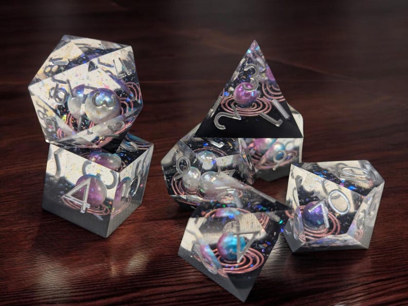 May include: Set of six iridescent dice with a galaxy theme. The dice are clear with embedded glitter and copper wire. Each die has a different number of sides, ranging from four to twenty.