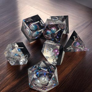 May include: A set of six clear resin dice with iridescent glitter and embedded pearls. The dice are numbered 1 through 6 and have a galaxy-themed design.