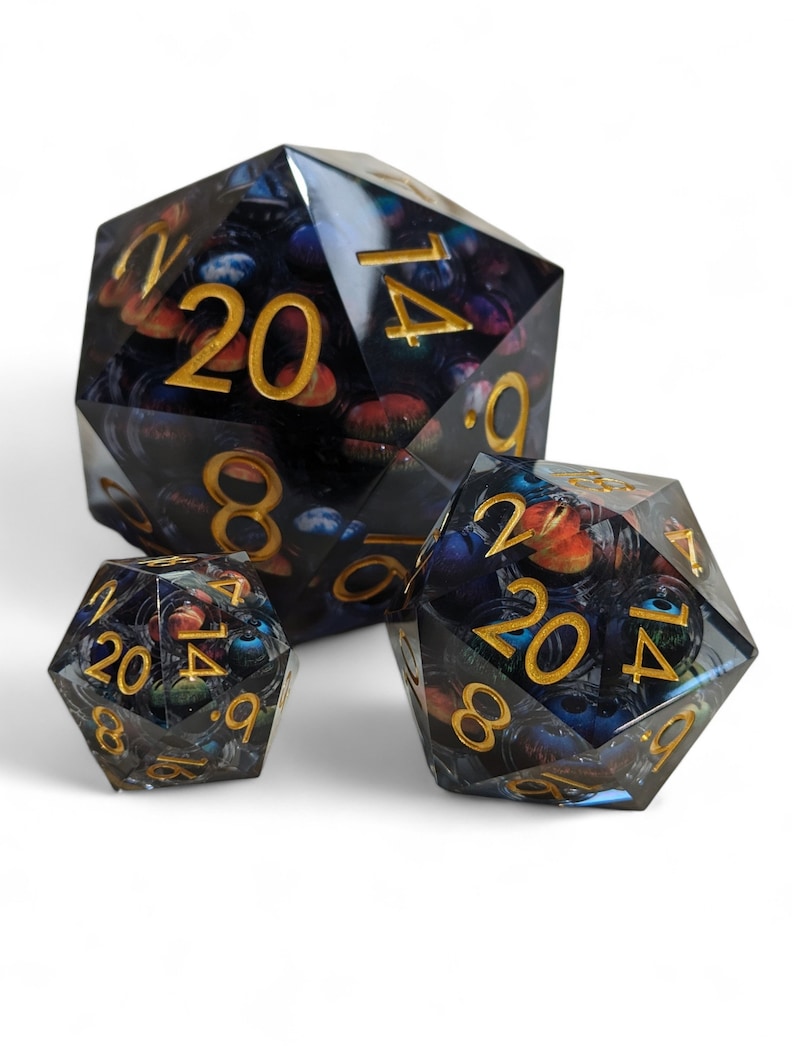 May include: Three black and blue dice with gold numbers. The dice are translucent and have a galaxy-like pattern. The numbers on the dice are 20, 14, 8, 9, 6, and 1.