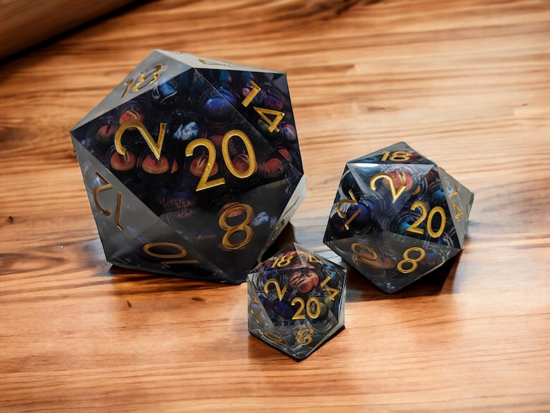 May include: Three clear, multi-sided dice with gold numbers and a galaxy-themed design. The dice are made of resin and have a translucent appearance.