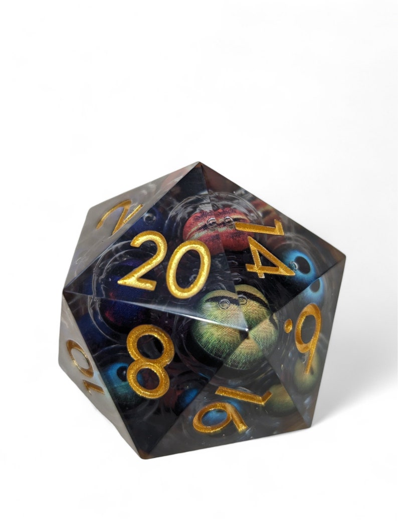 May include: A clear, multi-sided dice with gold numbers and a black and blue eye pattern. The dice is a 20-sided die.
