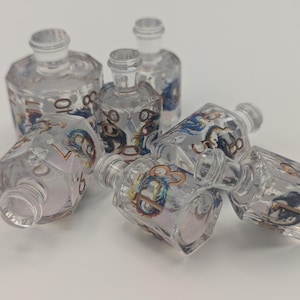 May include: A collection of clear glass bottles with decorative dragon and number designs. The bottles have clear stoppers and are arranged on a white surface. The bottles are of varying sizes and shapes.