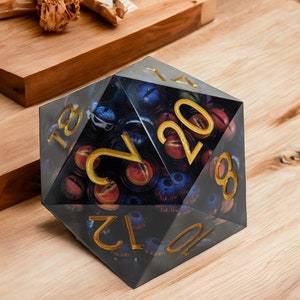 May include: A black and gold 20-sided die with a design of eyes and a dark background. The die is made of clear plastic and has gold numbers.