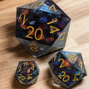 May include: Three clear, multi-sided dice with gold numbers and a galaxy-themed design. The dice are numbered 2, 4, 6, 8, 12, 14, 16, 18, 20.