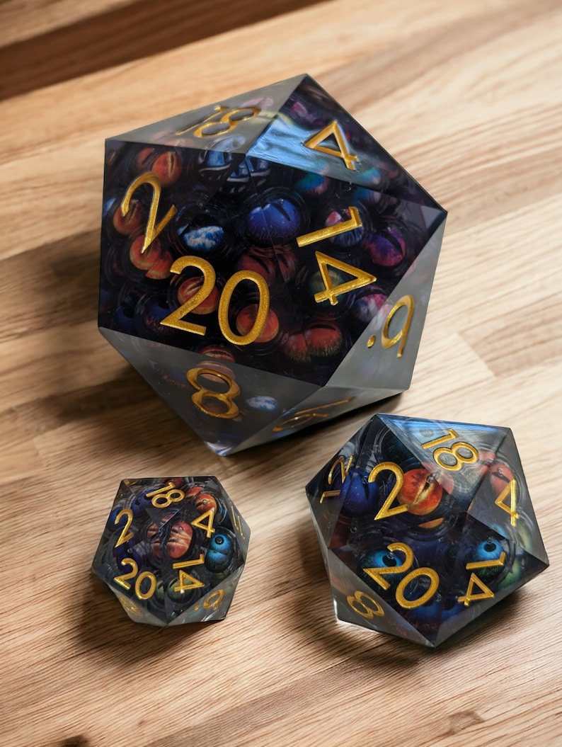 May include: Three clear, multi-sided dice with gold numbers and a galaxy-themed design. The dice are numbered 2, 4, 6, 8, 12, 14, 16, 18, 20.