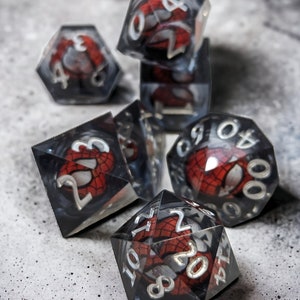 K&ouml;nnte beinhalten: Ein Satz von sechs schwarzen und roten W&uuml;rfeln mit einem Spider-Man-Design. Die W&uuml;rfel sind aus klarem Kunststoff und haben auf jeder Seite ein schwarzes und rotes Spider-Man-Design.
