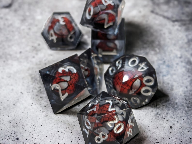 K&ouml;nnte beinhalten: Ein Satz von sechs schwarzen und roten W&uuml;rfeln mit einem Spider-Man-Design. Die W&uuml;rfel sind aus klarem Kunststoff und haben auf jeder Seite ein schwarzes und rotes Spider-Man-Design.