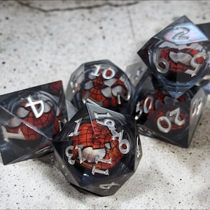 K&ouml;nnte beinhalten: Ein Satz von sechs transparenten W&uuml;rfeln mit einem roten und schwarzen Spider-Man-Design. Die W&uuml;rfel sind von 1 bis 6 nummeriert.