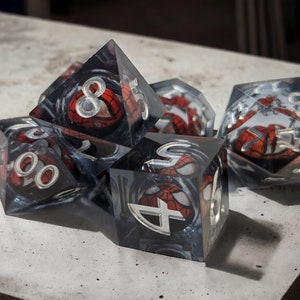 K&ouml;nnte beinhalten: Ein Satz von sechs transparenten, mehrseitigen W&uuml;rfeln mit einem Spider-Man-Design. Die W&uuml;rfel sind aus einem durchsichtigen Material gefertigt, und die Zahlen sind durch das Design sichtbar. Die W&uuml;rfel liegen auf einer grauen Oberfl&auml;che.
