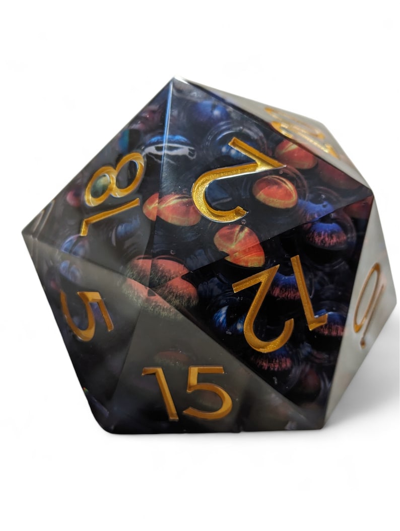 May include: A black and gold d20 dice with a galaxy-themed design. The numbers are in gold and the dice has a clear, iridescent finish.