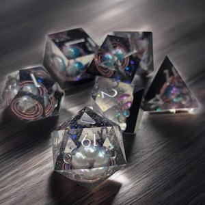 May include: A set of six iridescent dice with a galaxy theme. The dice are made of clear resin with embedded glitter and swirls. The numbers are visible on each face.