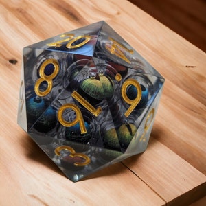 May include: A clear, multi-sided dice with gold numbers and a swirling, galaxy-like pattern inside. The dice is sitting on a wooden surface.