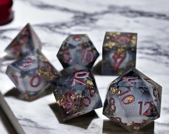 Peut inclure: Un ensemble de six dés noirs et blancs avec des chiffres rouges et des paillettes dorées. Les dés sont sur une surface en marbre blanc.