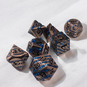 Könnte beinhalten: Ein Satz von sieben Kupfer- und blauen Würfeln mit schwarzen Zahlen. Die Würfel sind in verschiedenen Formen und Größen, darunter ein W20, W12, W10, W8, W6 und W4.