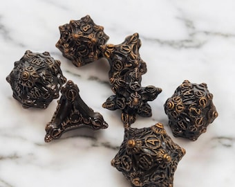 May include: A set of six black and gold metal dice with intricate designs. The dice are on a white marble surface.