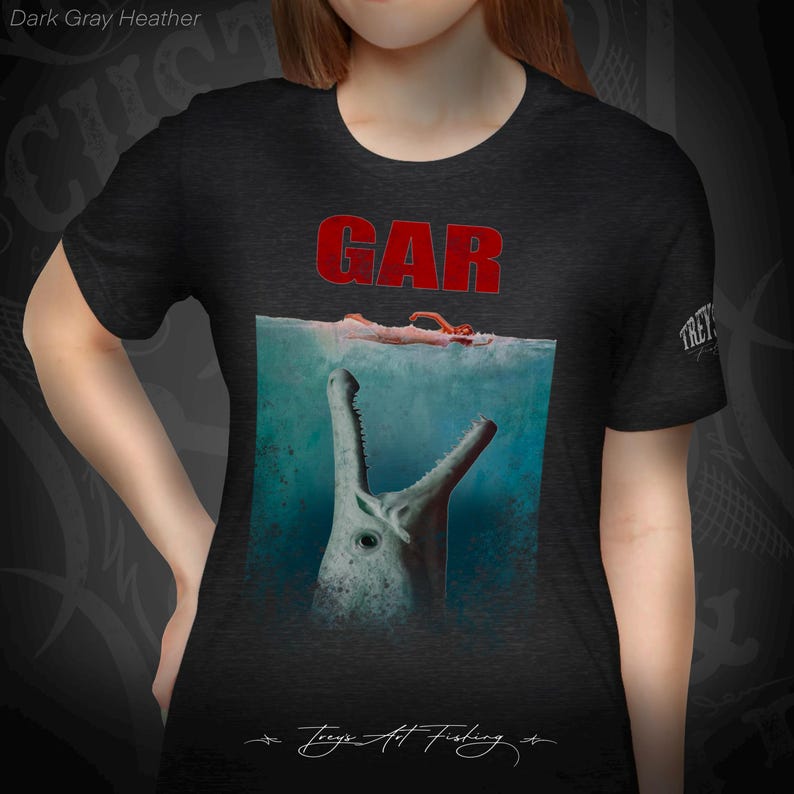 May include: A dark gray heather t-shirt with a graphic of a large fish with its mouth open, the word "GAR" in red letters above the fish, and the text "Treys Art Fishing" in cursive at the bottom.