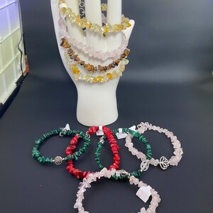 May include: A set of six gemstone bracelets with silver charms. The bracelets are made with chips of rose quartz, tiger's eye, malachite, and red coral.