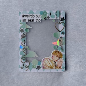 May include: A rectangular photo frame decorated with a light blue and white diamond pattern, featuring the text #weirdo but im real tho, a heart charm, feathers, stars, and a sticker of a person with blonde hair wearing a gold shirt.
