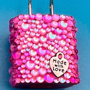 May include: A pink charger with a textured surface of iridescent beads. A small silver heart charm with the words "Made with Love" hangs from the charger. The charger has two silver prongs.