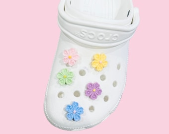 May include: White clogs with colorful flower charms. The charms are pink, yellow, green, purple, and blue.