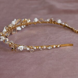 May include: A gold headband with white flowers and clear crystals. The headband is delicate and feminine.