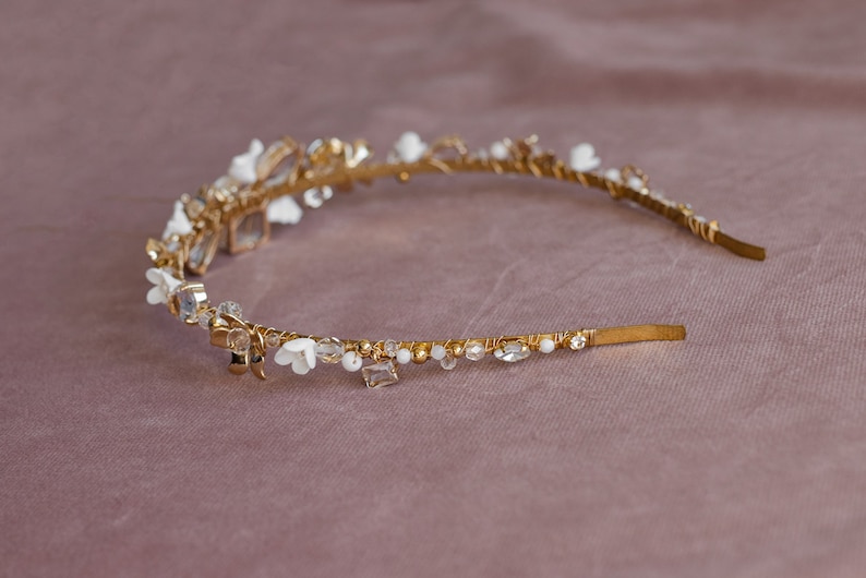 May include: A gold headband with white flowers and clear crystals. The headband is delicate and feminine.