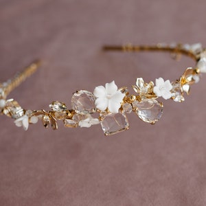 May include: A gold headband with white flowers and clear crystals. The headband is decorated with delicate gold leaves and is perfect for a wedding or special occasion.