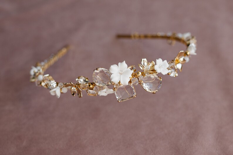 May include: A gold headband with white flowers and clear crystals. The headband is decorated with delicate gold leaves and is perfect for a wedding or special occasion.
