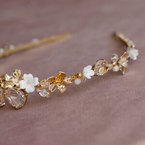 May include: A gold headband with white porcelain flowers and clear crystals. The headband is delicate and feminine.
