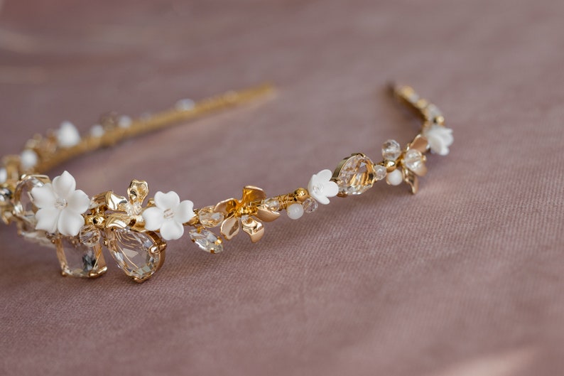 May include: A gold headband with white porcelain flowers and clear crystals. The headband is delicate and feminine.