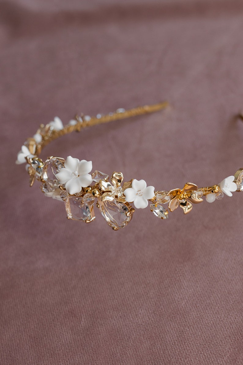 May include: A gold headband with white ceramic flowers and clear crystals. The headband is delicate and feminine.