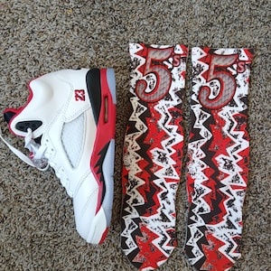 May include: White and red athletic shoe with black accents and the number "23" on the side. Beside it are two socks with a red and black lightning bolt design and the number "55".