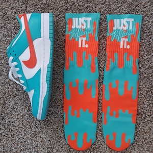 May include: A pair of turquoise and orange socks with the text "Just Do It." in white. The socks have a dripping paint design. A turquoise and white Nike shoe is also pictured.