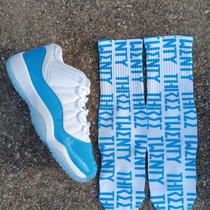 May include: A white and light blue trainer with a matching pair of socks. The socks are white with the words "TWENTY THREE" in light blue repeated vertically. The trainer has a light blue sole and accents.