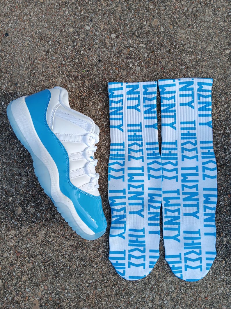 May include: A white and light blue trainer with a matching pair of socks. The socks are white with the words "TWENTY THREE" in light blue repeated vertically. The trainer has a light blue sole and accents.