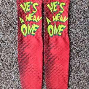 May include: A pair of red socks with a black snake skin pattern. The socks have the words "He's a mean one" written in yellow and green letters.