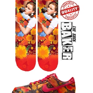 May include: A pair of red and orange socks with a floral pattern and a picture of a girl with long brown hair. The socks are next to a pair of red and orange Nike trainers with a floral pattern. The text "BAKER THE SOCK" is on a white sticker.