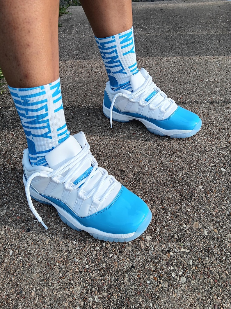 May include: White and light blue trainers with matching socks. The trainers have a glossy light blue toe cap and sole, with white laces and uppers. The socks are white with the text "UNITY" in light blue.