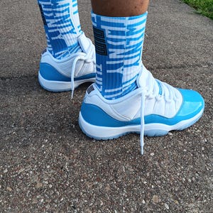May include: White and light blue trainers with matching blue and white socks. The socks display the word "UNITY". The trainers have a shiny light blue patent leather toe cap and a white sole.