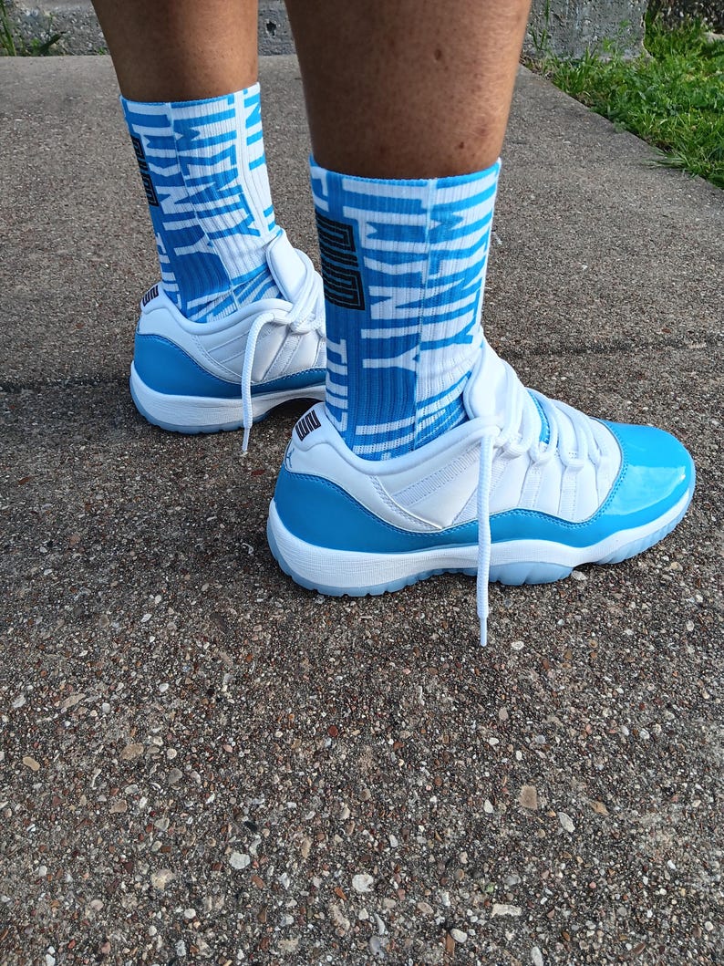 May include: White and light blue trainers with matching blue and white socks. The socks display the word "UNITY". The trainers have a shiny light blue patent leather toe cap and a white sole.