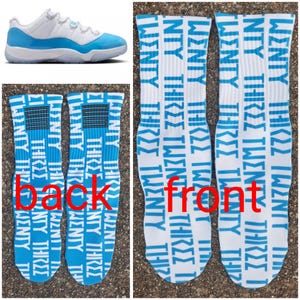 May include: White and light blue athletic shoes and two pairs of white socks. The socks feature the words "TWENTY THREE" in light blue repeated vertically. The back of the socks have a light blue and black design.