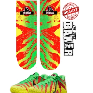 以下が含まれることがあります： 赤、黄、緑のデザインの「JA RASSIC」の文字が入った靴下と、緑と黄色のスニーカーのペア。スニーカーと靴下は白い背景に表示されています。