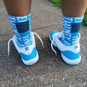 May include: White and light blue sneakers with matching blue and white patterned socks. The sneakers have white laces and a light blue heel. The socks feature a black and blue design.