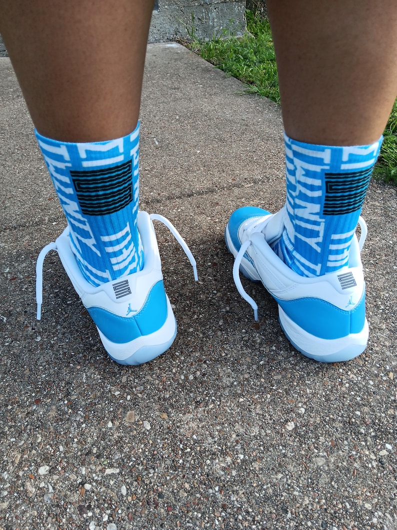 May include: White and light blue sneakers with matching blue and white patterned socks. The sneakers have white laces and a light blue heel. The socks feature a black and blue design.