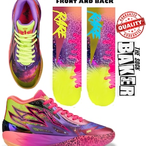 以下が含まれることがあります： 銀河柄とピンクのアクセントが施された、マルチカラーのバスケットボールシューズのペア。シューズには黒いスウッシュロゴと側面に「Rage」の文字が書かれている。シューズは白い背景に、銀河柄のソックスと側面に「The Sock Baker」の文字が書かれたソックスのペアが置かれている。