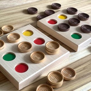 May include: Two wooden game boards with circular depressions for playing a game. The boards have red, yellow, and green colored circles. The boards are surrounded by wooden game pieces with concentric circles.
