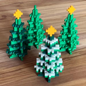 Könnte beinhalten: Vier pixelige Weihnachtsbäume in Grün- und Weißtönen, jeder mit einem gelben Stern gekrönt. Die Bäume sind auf einer Holzoberfläche angeordnet und zeigen ein festliches Urlaubsthema.